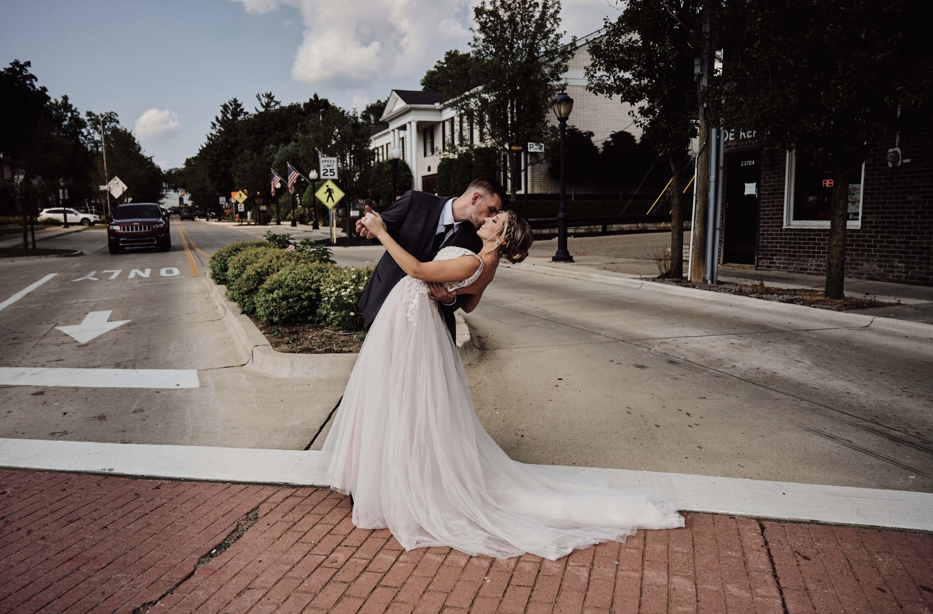 A groom dips the bride in the middle of the crosswalk of a street in Farmington, Michigan